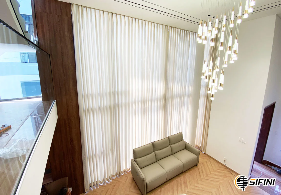 Rèm vải màu trắng kem che cửa kính cao trong phòng khách hiện đại, bên cạnh ghế sofa màu be