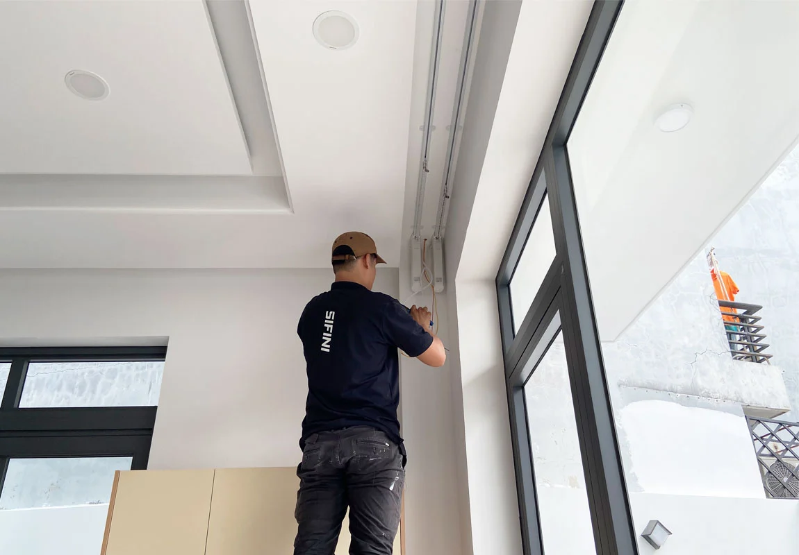 Kỹ thuật viên lắp đặt ray rèm cửa tự động sát trần cạnh cửa kính lớn
